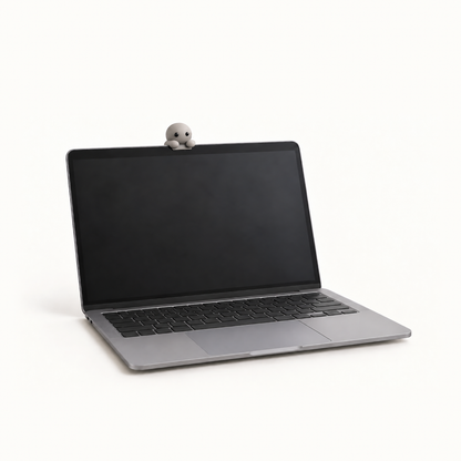 The MacBook Perch in the Stone colourway, a slim matte grey ledge on a laptop lid, with a Corbie peeking over its edge at the owner.